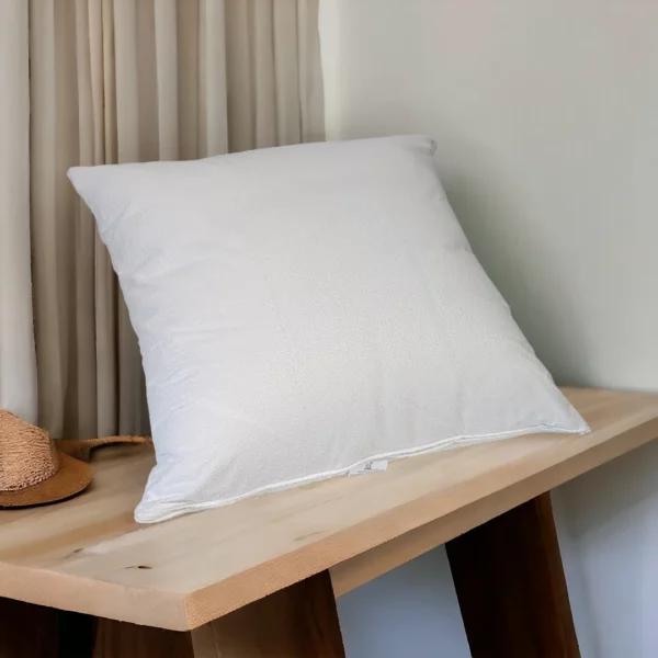 Taie d'oreiller en coton blanc imperméable posée sur une console en bois clair dans une chambre d'hôtel épurée.