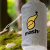 Sac de transport gris de la marque Mash avec son logo distinctif, posé sur de la mousse en forêt.