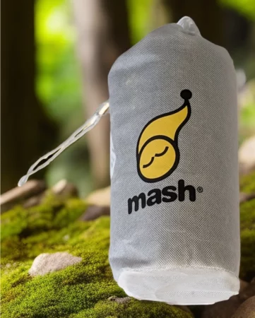 Sac de transport gris de la marque Mash avec son logo distinctif, posé sur de la mousse en forêt.