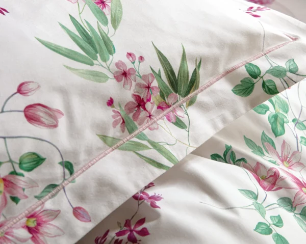 Gros plan sur la taie d'oreiller Aura d'Anne de Solène en percale de coton bio, détaillant les motifs floraux et la finition couture.