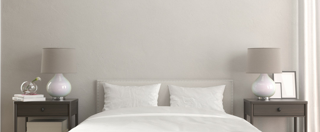Chambre à coucher épurée avec un grand lit King Size blanc, entouré de deux tables de chevet munies de lampes à abat-jour gris.