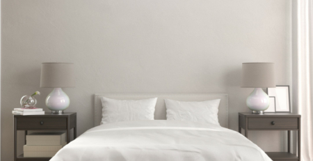 Chambre à coucher épurée avec un grand lit King Size blanc, entouré de deux tables de chevet munies de lampes à abat-jour gris.