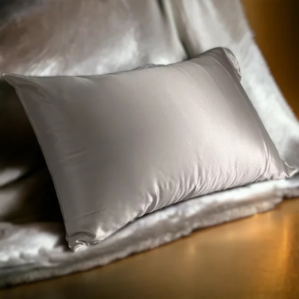 Taie d'oreiller soyeuse de couleur nacre taille 50x75, reflétant une lumière douce sur un lit luxueux.