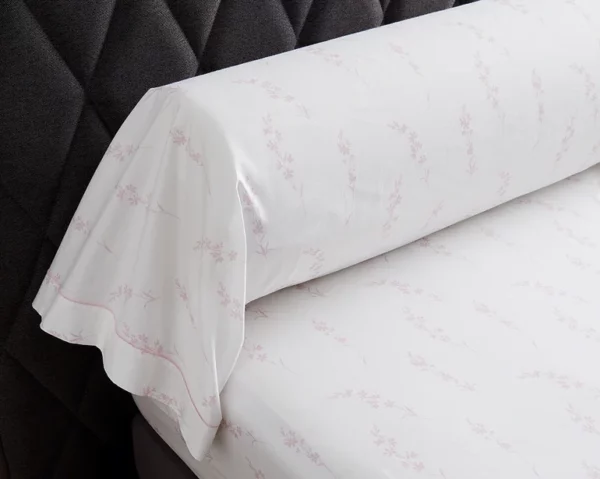 Taie de traversin Aura en percale de coton bio avec imprimés floraux, posée sur un lit, mise en valeur par un fond sombre, offerte par Litex.