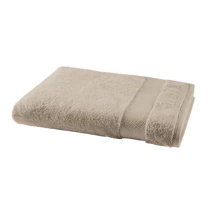 Lot de linge de toilette Pétale Roseau plié sur une étagère en bois avec une bouteille d'huile corporelle et un savon. Le jet d'eau de la douche est visible en arrière-plan.