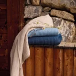 Plaids Évian drapés et superposés dans un décor rustique en bois et pierre naturelle.