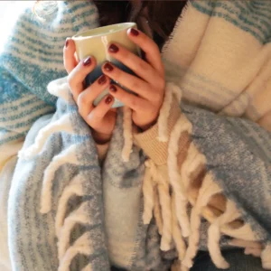 Femme enroulée dans un plaid rayé bleu effet mohair tenant une tasse